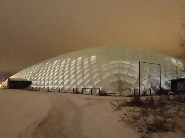 A large air-supported dome in a field of snow and a sky of orange.